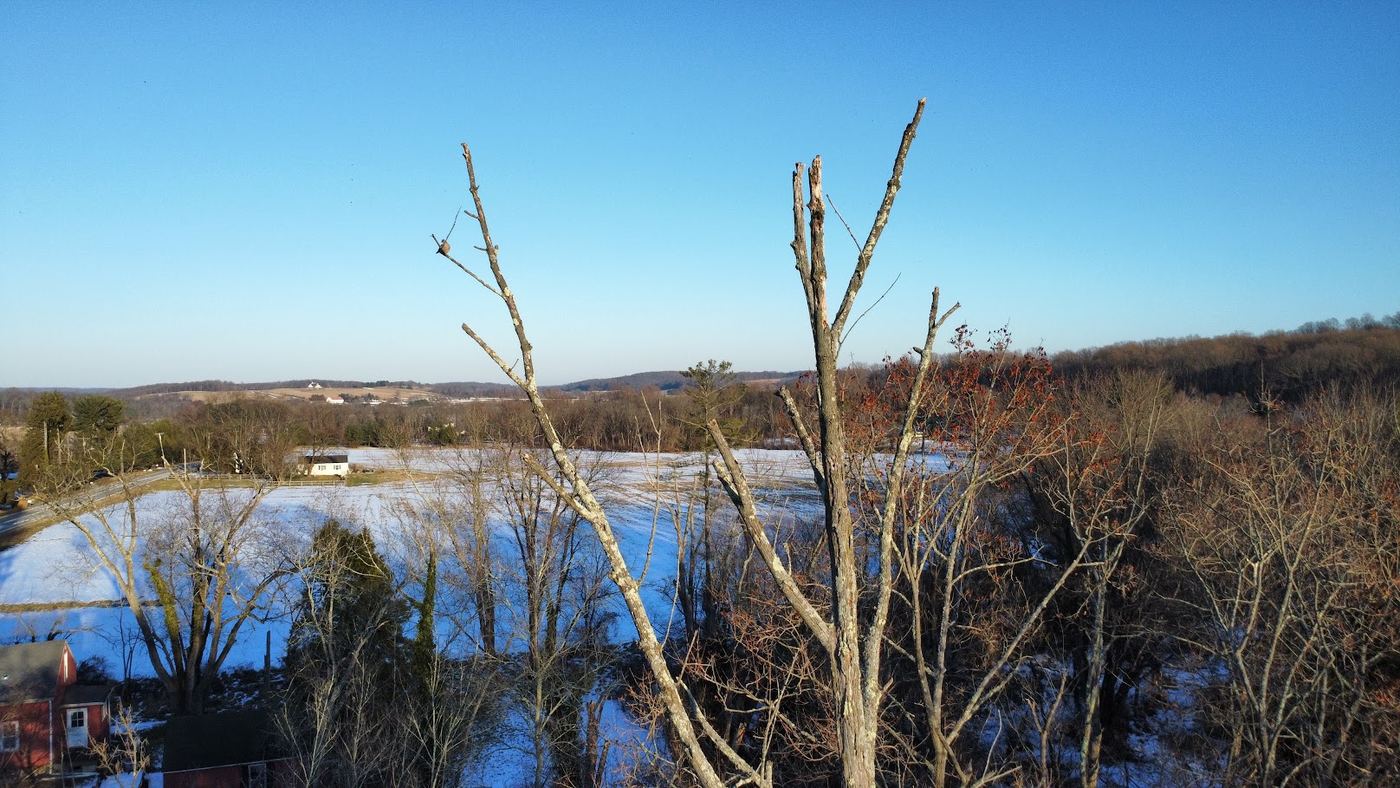 Drone view over snow-covered farm fields, woods and rolling hills under a clear blue sky