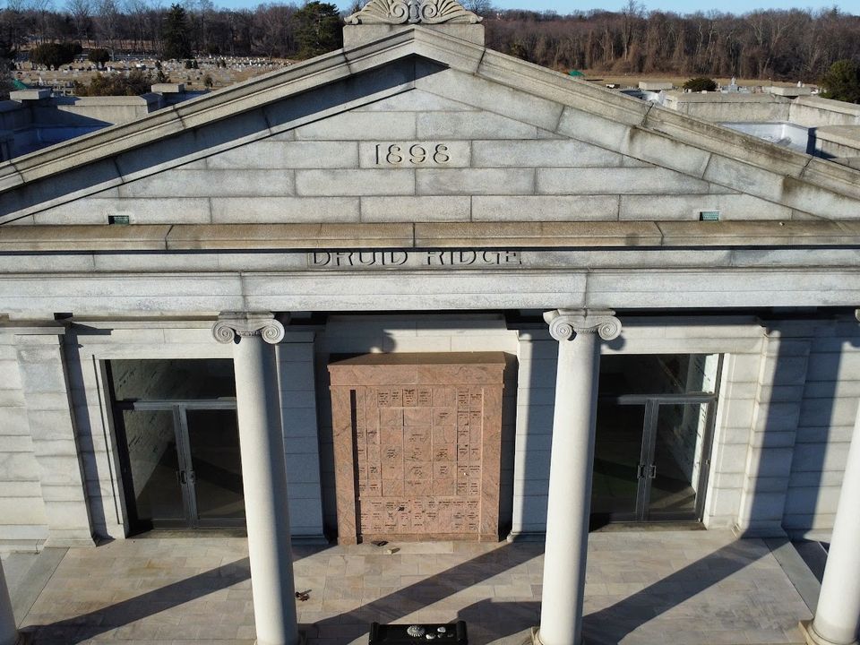 Close-up drone view of a columned stone facade with 1898 carved into its peak